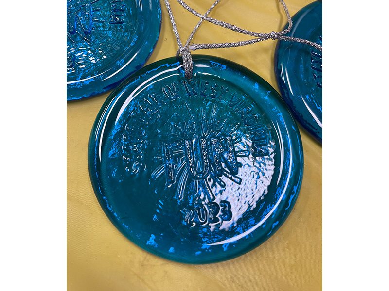 Blue glass ornament on silver string with State Fair of West Virginia Cue the Fun 2023 logo